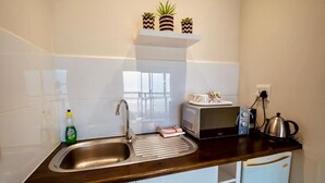 Eine Küche mit Spüle aus Edelstahl, einer Mikrowelle, einem Wasserkocher und einem kleinen Kühlschrank.