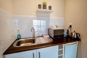 A kitchen with a stainless steel sink, a microwave, a kettle, and a small refrigerator. - Interlaken Guest House (Wilderness)