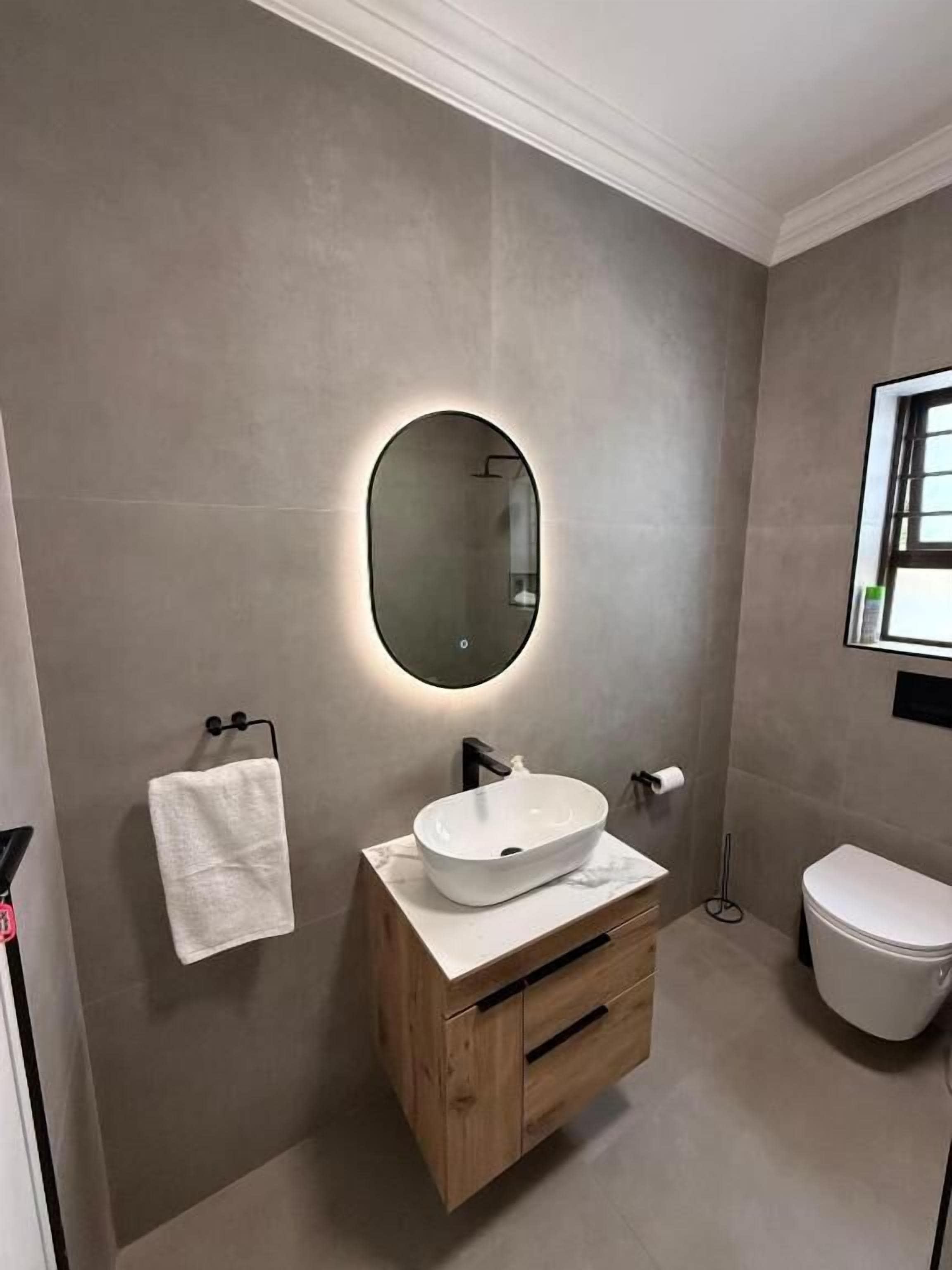 A modern bathroom with a wooden vanity, a round mirror, and a white toilet.