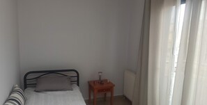 A small, single-bed room with a wooden nightstand, a radiator, and a window with sheer curtains. - Amazing View- Heart of the City (Thessaloniki)