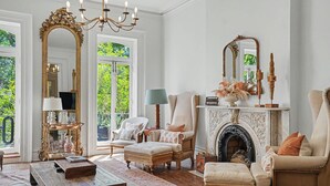 Uma sala de estar ampla com lareira, dois poltronas, um sofá, uma mesa de centro e um espelho grande.