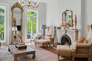 Uma sala de estar ampla com lareira, dois poltronas, um sofá, uma mesa de centro e um espelho grande.