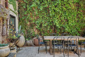 Eine Terrasse im Freien mit einem Holztisch und -stühlen, umgeben von Topfpflanzen und einer mit Grün bewachsenen Wand.