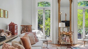Sala de estar com sofá branco, um espelho grande e vista para o verde lá fora.