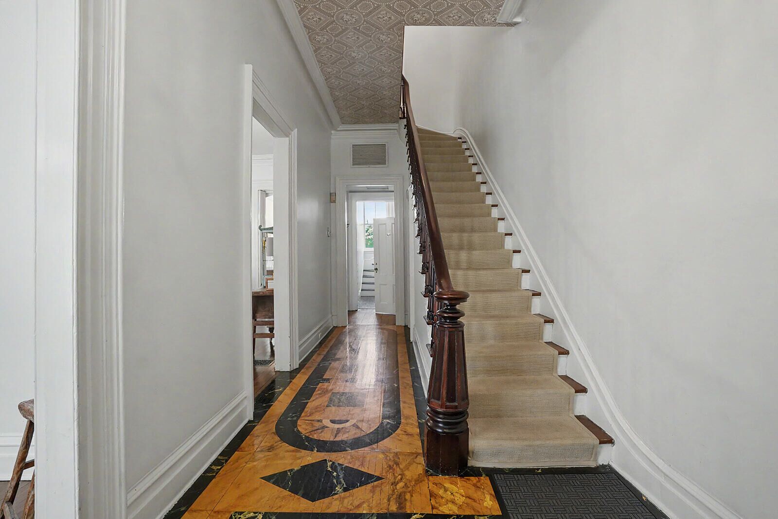 A hallway with a wooden staircase, a patterned floor, and white walls.