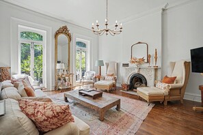Ein geräumiges Wohnzimmer mit Kamin, großen Fenstern und einer Kristallleuchter.