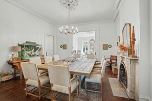 Ein Esszimmer mit einem großen Holztisch, mehreren Stühlen, einer Kristallleuchtre, einem Kamin und einem grünen Vogelkäfig.
