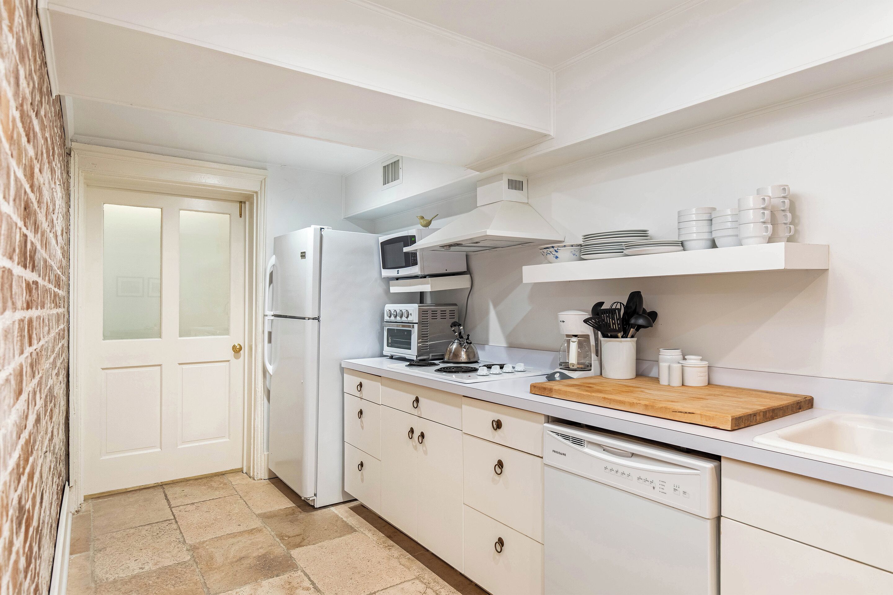 A kitchen with white cabinetry, a microwave, a toaster, a wooden cutting board, and a dishwasher.