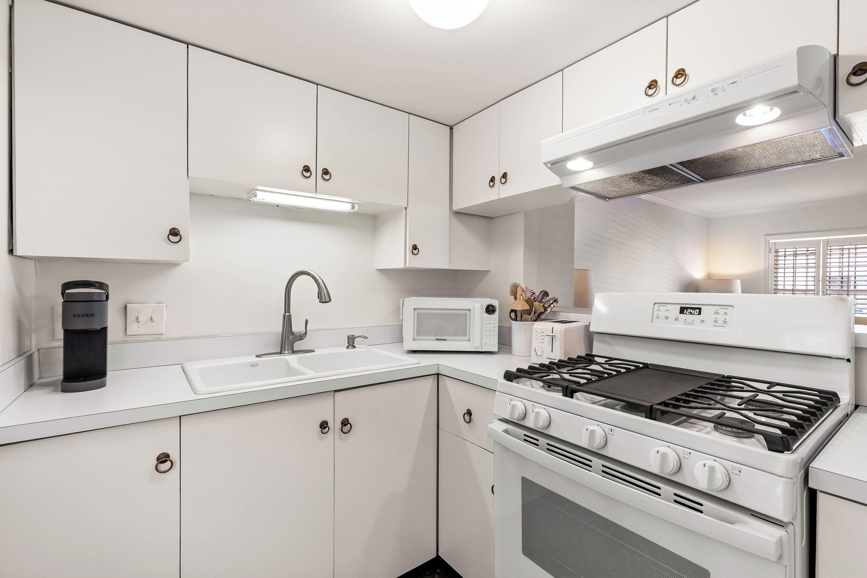 Una cocina moderna con armarios blancos, microondas integrado, estufa a gas y cafetera.