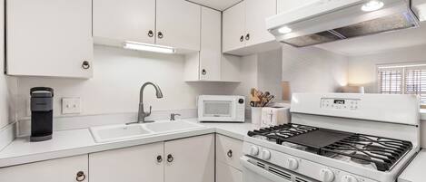Una cocina moderna con armarios blancos, microondas integrado, estufa a gas y cafetera.