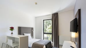 Ett hotellrum med en säng, ett skrivbord, en stol, en tv och ett fönster med gardiner.