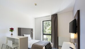 A hotel room with a bed, desk, chair, TV, and a window with curtains. - Adonis Dijon Single Apartment (Dijon)