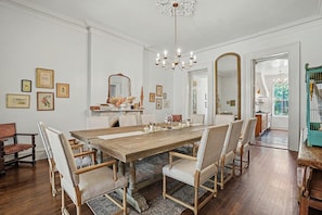Ein Esszimmer mit einem großen Holztisch, gepolsterten Stühlen, einer Kandelaber und gerahmten Bildern an den Wänden.