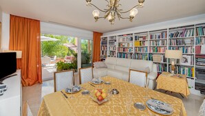 A well-lit room with a dining table set for two, a white sofa, and a large bookshelf filled with books. - Real1b - Beautiful apt With Tropical Terrace (Marbella)
