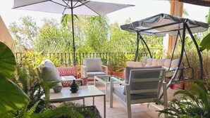 An outdoor patio with a swing chair, a table, and a cushioned bench. - Real1b - Beautiful apt With Tropical Terrace (Marbella)