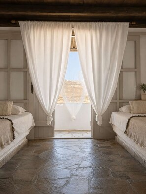 Ein Zimmer mit zwei Betten, Steinboden und Blick durch transparente Vorhänge.