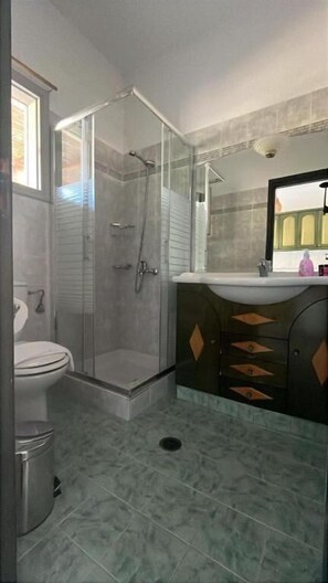 A bathroom with a glass shower enclosure, a toilet, a sink with a mirror, and a cabinet with drawers. - Paros Casa Prive - Poseidon Shared Pool Nest (Ag Charalambos)
