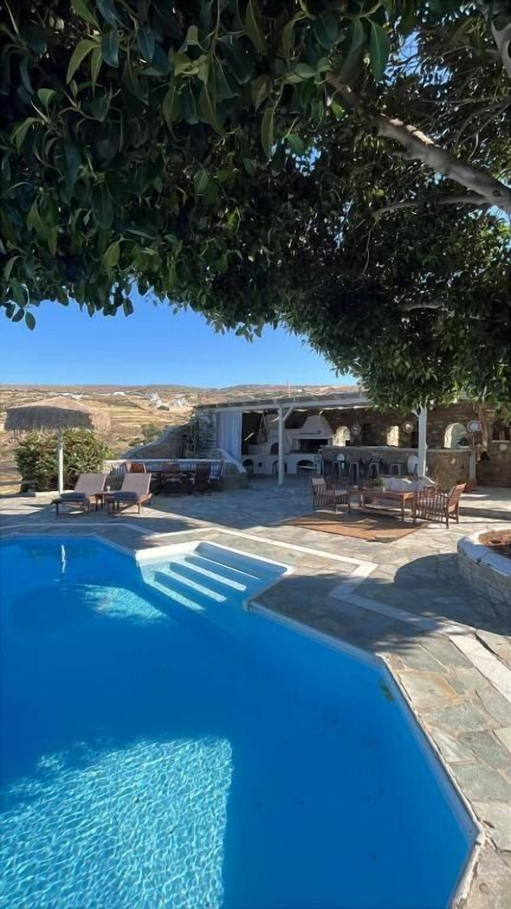 A swimming pool with a stone deck, outdoor furniture, and a view of the landscape.
