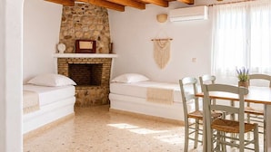 Una habitación con chimenea de piedra, vigas de madera en el techo, una mesa de comedor con sillas y un sofá blanco.