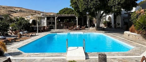 Ein Pool mit Liegestühlen und einem Tisch, umgeben von Steinböden und einem großen Baum.