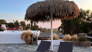 Un espacio al aire libre con suelo de piedra, dos sillones de relax y un toldo de paja.