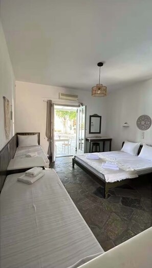 A hotel room with two beds, a dining table, a chair, a hanging light fixture, and a view of the outdoors. - Paros Casa Prive - Iria Shared Pool Nest (Ag. Charalampos)