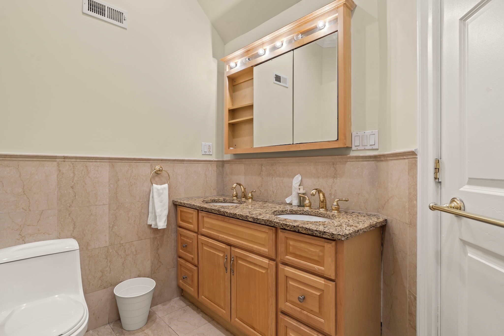 Un bany amb vàter, un lavabo amb calaixera, un mirall amb llums i una porta.