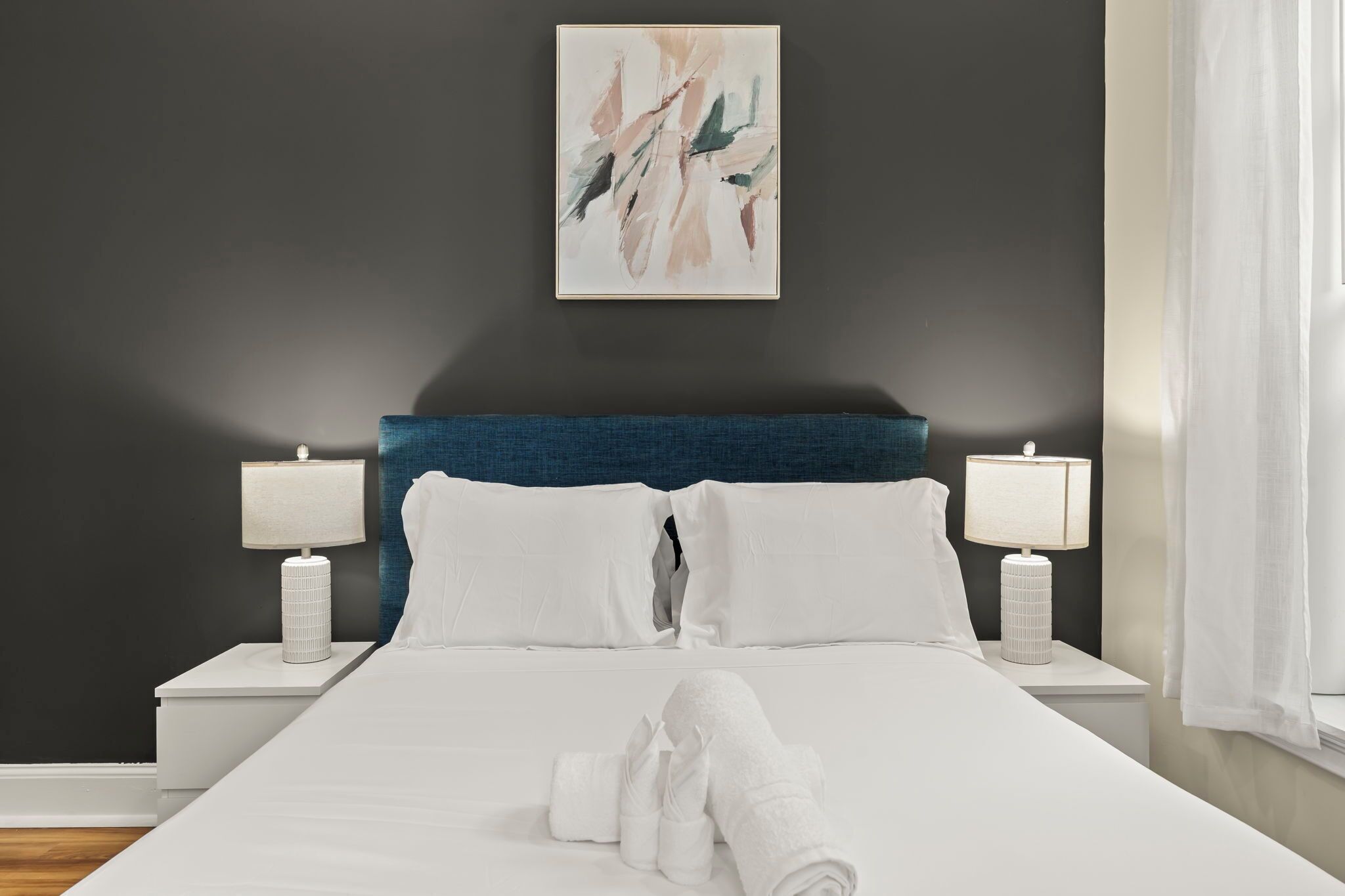 Une chambre d’hôtel avec un lit, deux tables de chevet avec des lampes, un tableau au mur et une fenêtre avec des rideaux.