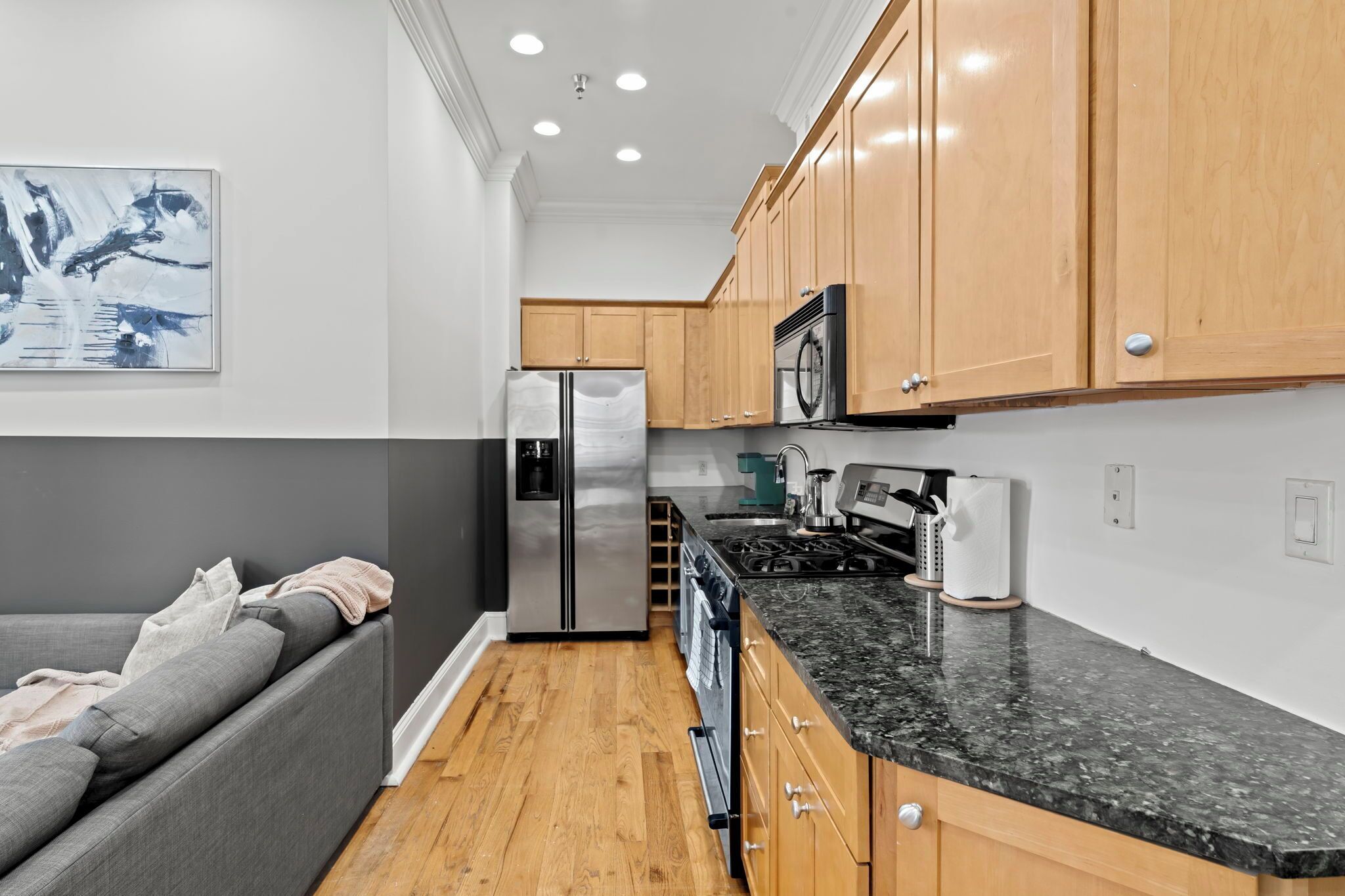 A modern kitchen with wooden cabinets, a stainless steel refrigerator, and a black granite countertop.