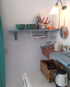 Eine Küche mit Regalen, auf denen Schüsseln, Kochutensilien und ein Wasserkocher stehen.