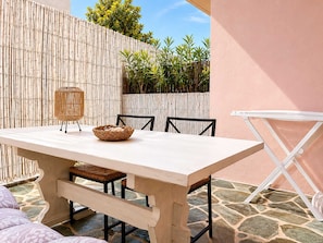 Ein Tisch mit Stühlen, ein gewebter Korb und ein Korbstuhl auf einer Terrasse mit Bambuszaun und Steinboden.