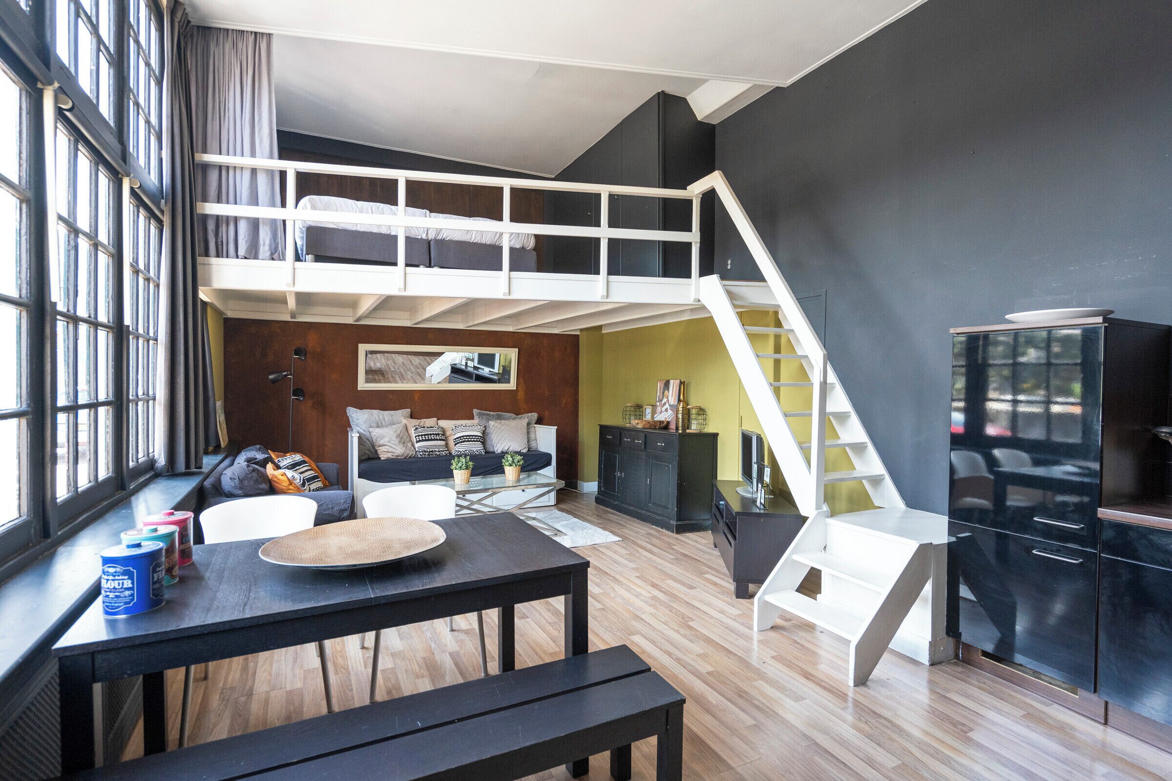 A loft-style room with a bunk bed, a dining table, and a staircase.