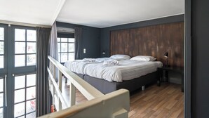 Ein Schlafzimmer mit Bett, Schreibtisch, Lampe und Blick ins Freie.