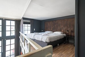 A bedroom with a bed, a desk, a lamp, and a view of the outside. - De IJsfabriek - Industrial loft studio in Zandvoort (Zandvoort)