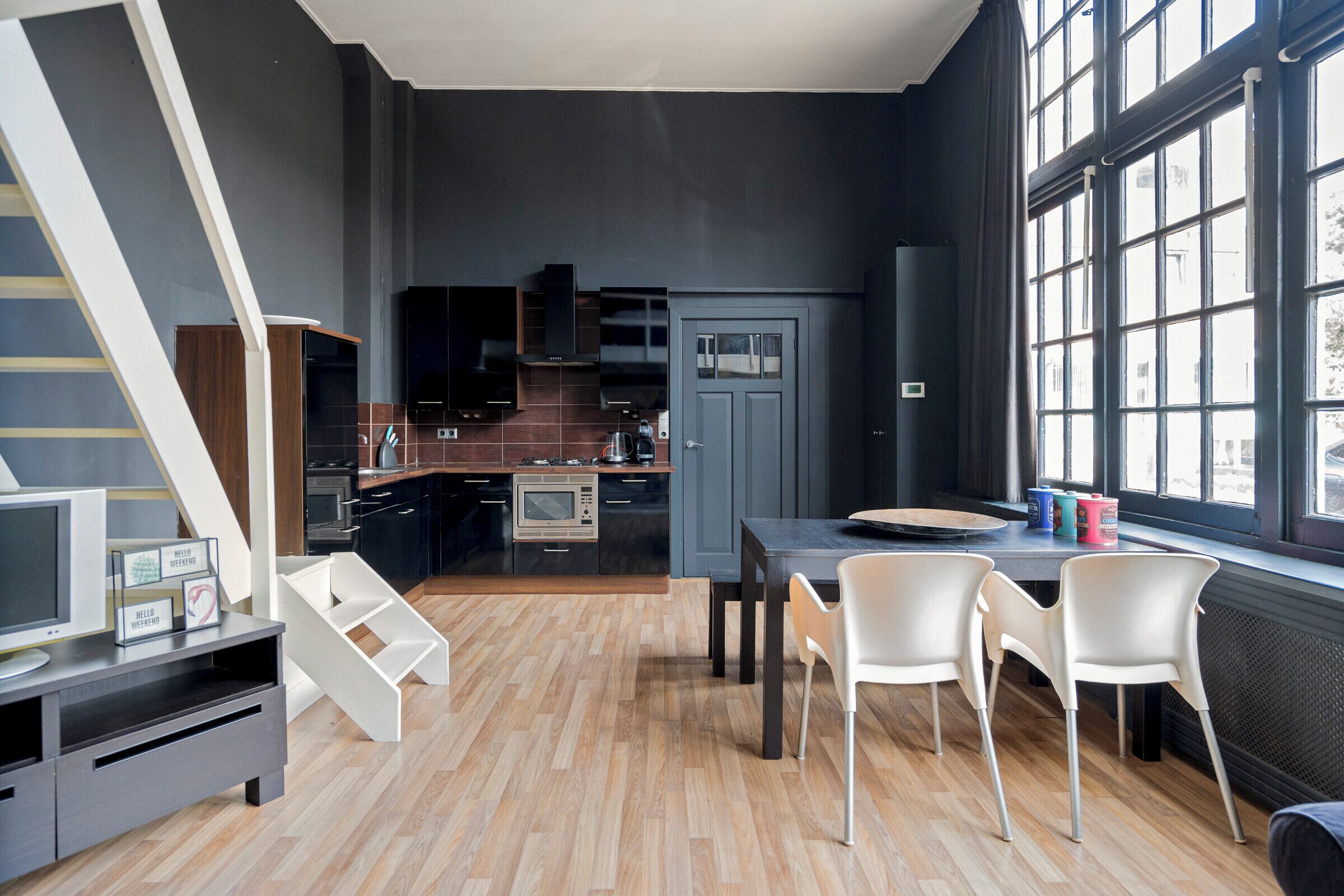 A modern kitchen with dark cabinetry, a dining area with a table and chairs, and a staircase.