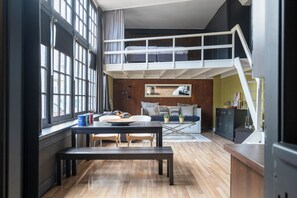 A loft-style room with a bunk bed, a dining table with chairs, a kitchen area, and a large window. - De IJsfabriek - Industrial loft studio in Zandvoort (Zandvoort)