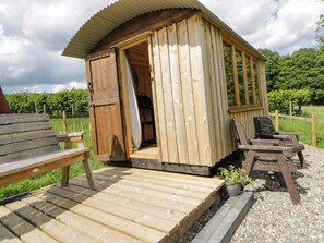 A wooden cabin with a door open, revealing a kitchen area, and two wooden chairs outside. - The Little Shepherds Hut With a View (Builth Wells)