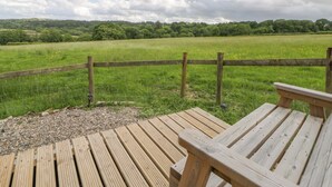 Eine Holzterrasse mit Blick auf ein Wiesenfeld und einen Holzzaun.