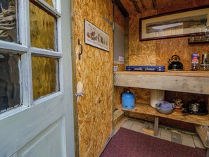 A kitchen with wooden walls, a gas stove, a kettle, and a shelf with kitchen utensils. - The Little Shepherds Hut With a View (Builth Wells)