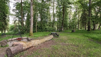 A picnic area with a table, benches, and a swing set in a wooded park.