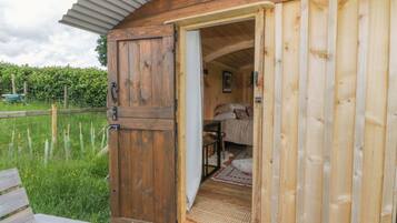 A wooden cabin with an open door revealing a bedroom with a bed, pillows, and a small table.