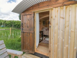 Una cabaña de madera con la puerta abierta que muestra un dormitorio con cama, almohadas y una mesita.