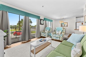 A living room with a green sofa, a white coffee table, patterned armchairs, and a view of a red car outside. - B148 at the Myrtle Beach Resort (Myrtle Beach)
