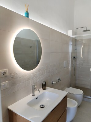 Un baño moderno con un espejo redondo, un lavabo, un inodoro y una ducha con mampara de vidrio.