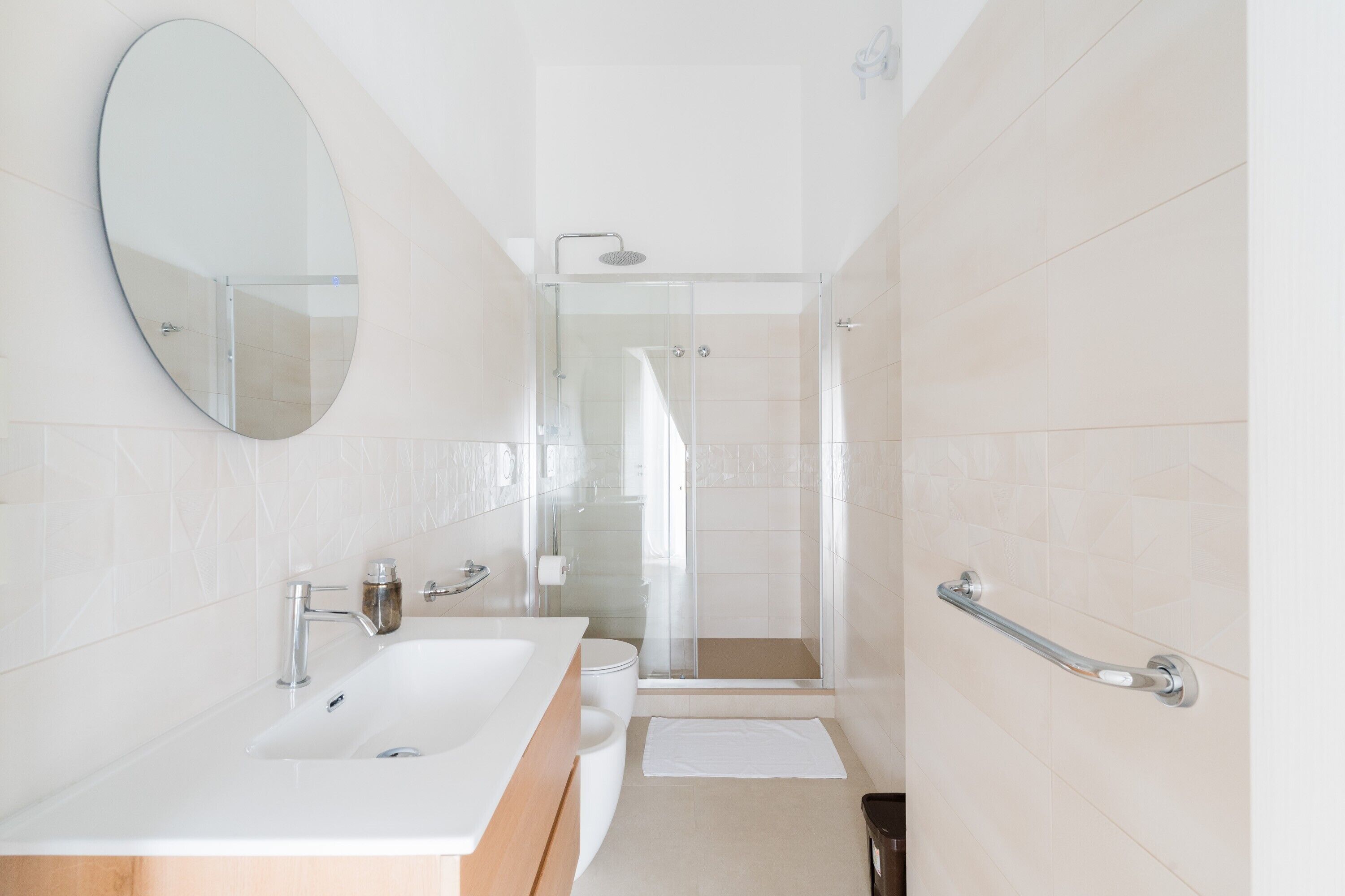 Ein modernes Badezimmer mit großem Spiegel, Waschbecken, Dusche und einer Haltestange.