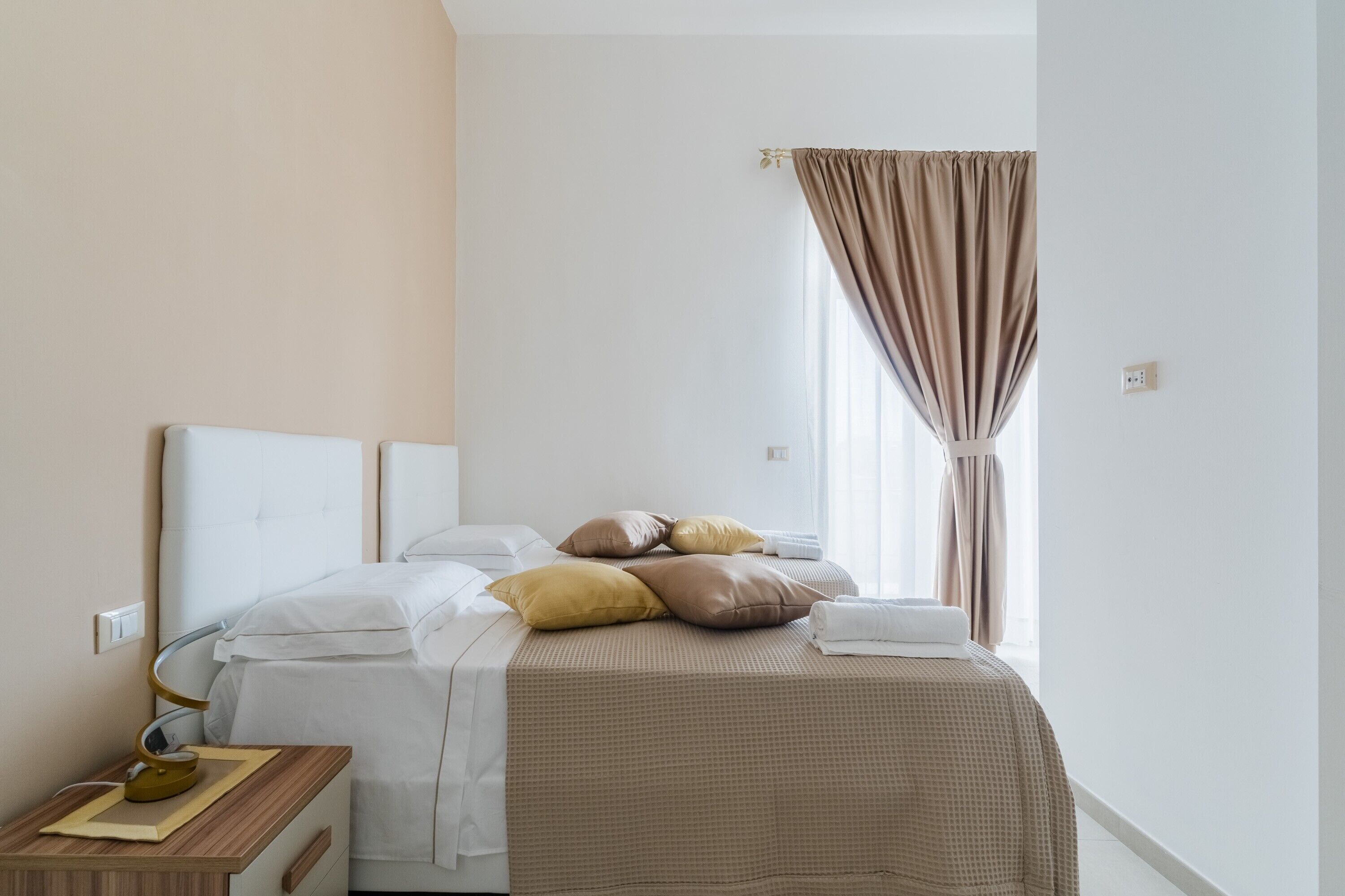 Et hotelværelse med seng, natbord, lampe og gardiner.