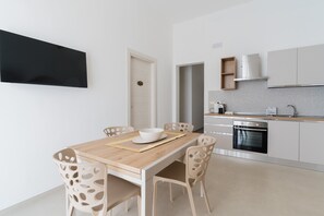 Una cocina moderna con armarios blancos, horno empotrado y una zona de comedor con mesa y sillas de madera.