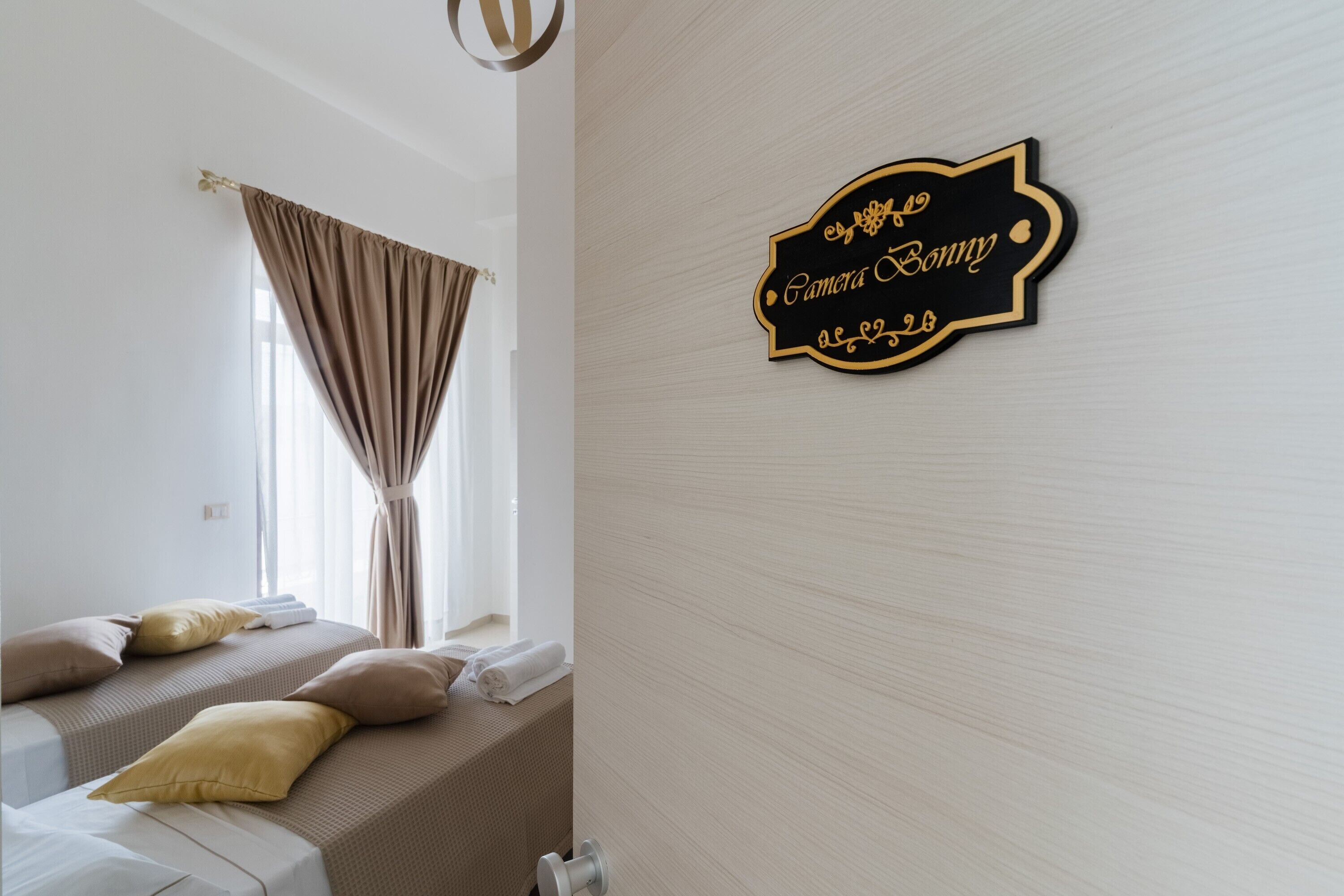 Una habitación de hotel con una cama, almohadas, una ventana con cortinas y un cartel en la pared.