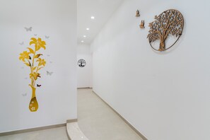 Um corredor com um ornamento de árvore na parede, um vaso com flores e borboletas.