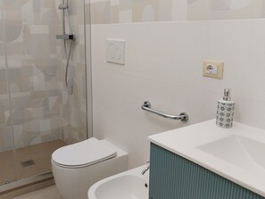 Un bany amb dutxa, vàter, bidé i un lavabo amb penjador de tovalloles.